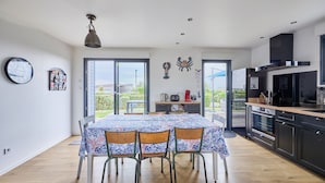 A modern kitchen with a dining area, featuring a large table with chairs, a view to the outdoors, and a variety of appliances.