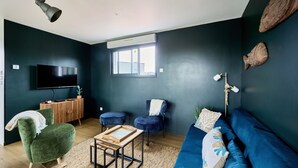 A modern living room with a dark green sofa, blue armchairs, a wooden coffee table, and a flat-screen TV mounted on the wall.