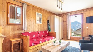 A wooden-furnished room with a red sofa, a wooden table, a TV, and a mountain view.