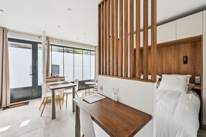 Une chambre d’hôtel moderne, dotée d’un bureau en bois, d’un lit avec une literie blanche et d’une grande fenêtre donnant sur l’extérieur.