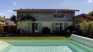 Une maison avec une piscine, une terrasse avec des chaises et un petit jardin.