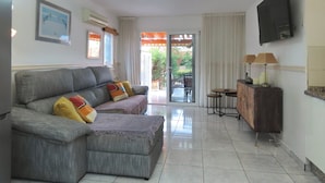 Un salón con un sofá gris, un televisor montado en la pared y un ventanal corredero que da a un área exterior.