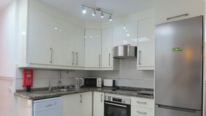 Una cocina moderna con armarios blancos, un refrigerador de acero inoxidable, un lavavajillas, un microondas y una estufa.