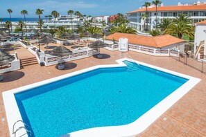 Relax by the resort pool surrounded by lounge chairs and umbrellas, with a clear view of the surrounding architecture and landscape.