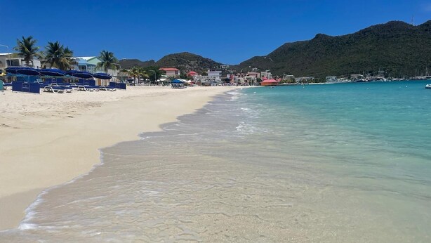 A beach with clear turquoise water, sandy shore, and buildings in the background. - 2-bedroom apartment, sea view terrace in marvelous Point Blanche, 2 BA, AC, WIFI (Pointe Blanche)