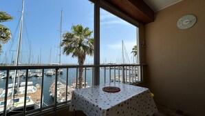 A balcony with a table and chairs, overlooking a marina with boats and palm trees. - Charming studio with sea view, Gruissan (Gruissan)