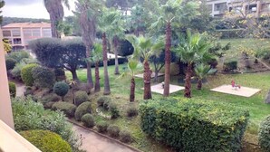 A well-maintained garden with various trees and shrubs, a paved pathway, and a small seating area. - Apartment with pool near the sea (Sanary-sur-Mer)
