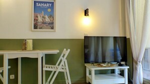 A room with a green and white color scheme, a white table with a chair, a flat-screen TV on a stand, and a poster on the wall. - Apartment with pool near the sea (Sanary-sur-Mer)