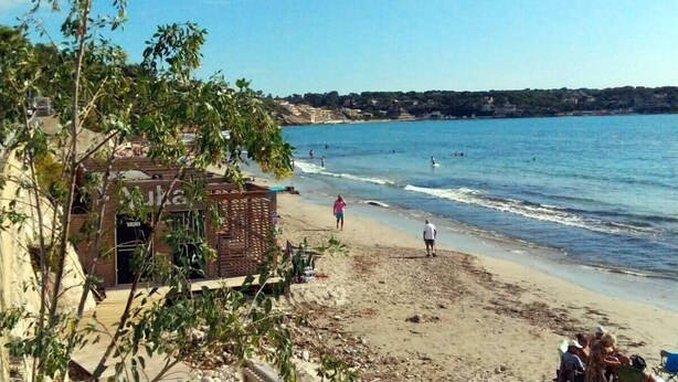 A beach with a building on the left, people walking on the sand, and the sea in the background. - Apartment with pool near the sea (Sanary-sur-Mer)
