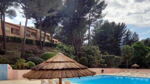 A swimming pool with lounge chairs and a thatched umbrella. - Apartment with pool near the sea (Sanary-sur-Mer)