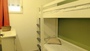 Ein Stockbett mit grünem Kopfteil, ein kleiner Nachttisch mit einem Korb und ein roter Vorhang.