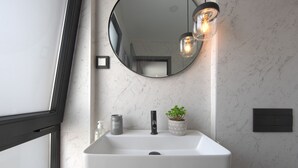 Ein Badezimmer mit einem weißen Waschbecken, einem runden Spiegel, einer Topfpflanze und einer Lampe.