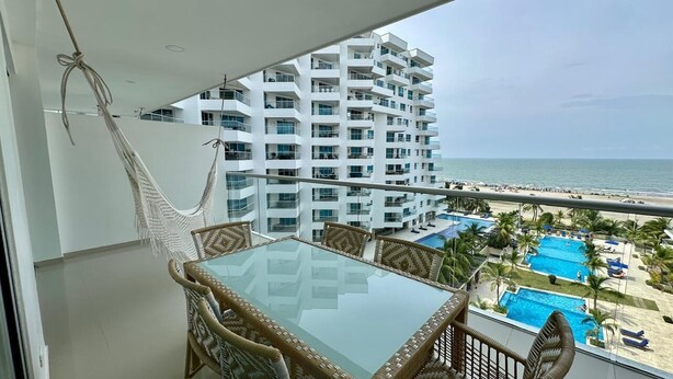 A balcony with a glass table and wicker chairs, overlooking a beach and a pool area. - Charming 2-bedroom apartment with WiFi, AC in amazing Cartagena De Indias (Cartagena De Indias)