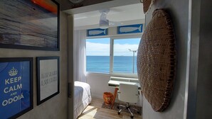 Ein Zimmer mit einem Bett, einem Schreibtisch, einem Stuhl, einem großen gewebten Wandbehang und Meerblick durch ein Fenster.