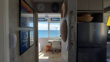 Una cocina con refrigerador, teléfono y vista al mar por una ventana.