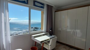 Una habitación con un ventanal que ofrece vistas al océano, un escritorio con una lámpara y un armario.