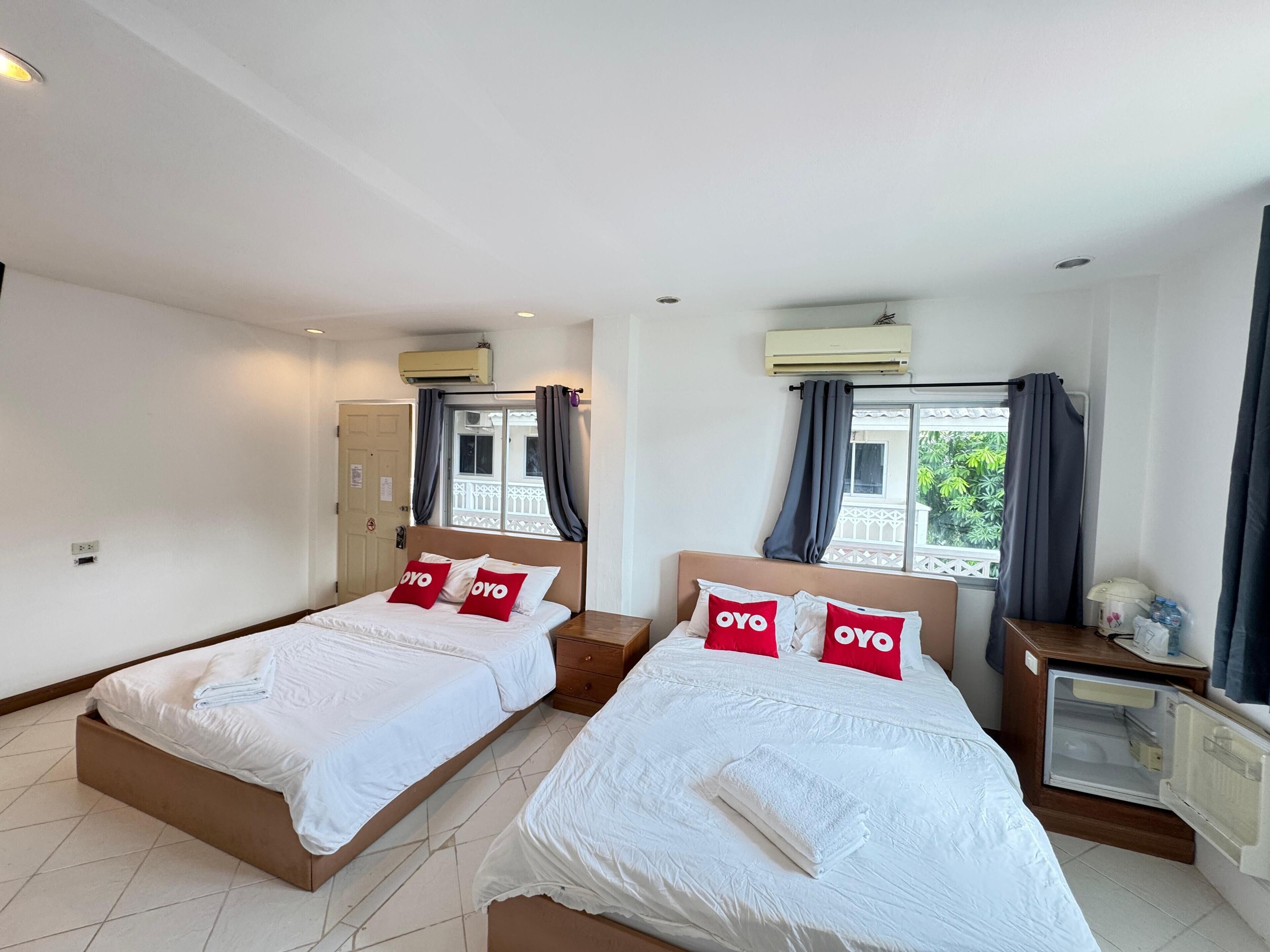 A hotel room with two beds, each with white bedding and red pillows, a small bedside table, a nightstand, and a window with curtains.