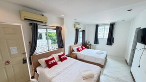 A hotel room with two beds, each with white bedding and red pillows, a TV on the wall, and air conditioning units above the beds. - Blue Horizon (Hua Hin)