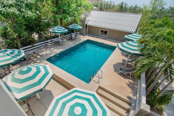 A rectangular swimming pool with a tiled deck, surrounded by lounge chairs and green-striped umbrellas. - Blue Horizon (Hua Hin)