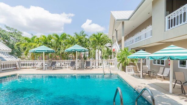 A swimming pool with lounge chairs and umbrellas, surrounded by palm trees and a building with balconies. - Blue Horizon (Hua Hin)