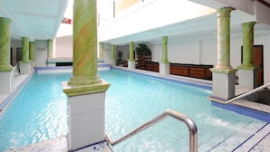 Une piscine intérieure dotée de colonnes en marbre, d’un sol carrelé et d’un espace avec des bancs en bois.