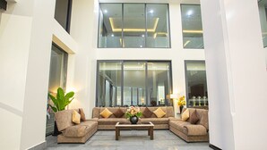 A spacious lobby with a high ceiling, a central seating area with a sofa and coffee table, and large windows providing natural light. - Nalada Hotel (Ou Chrov)