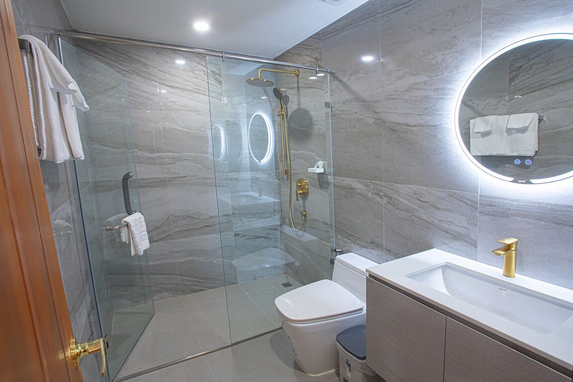 Un baño moderno con ducha envuelta en vidrio, inodoro blanco y tocador con grifo dorado.