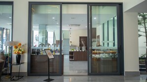 A modern hotel lobby with a reception desk, a vase of flowers, and a view of the kitchen area through glass doors. - Nalada Hotel (Ou Chrov)