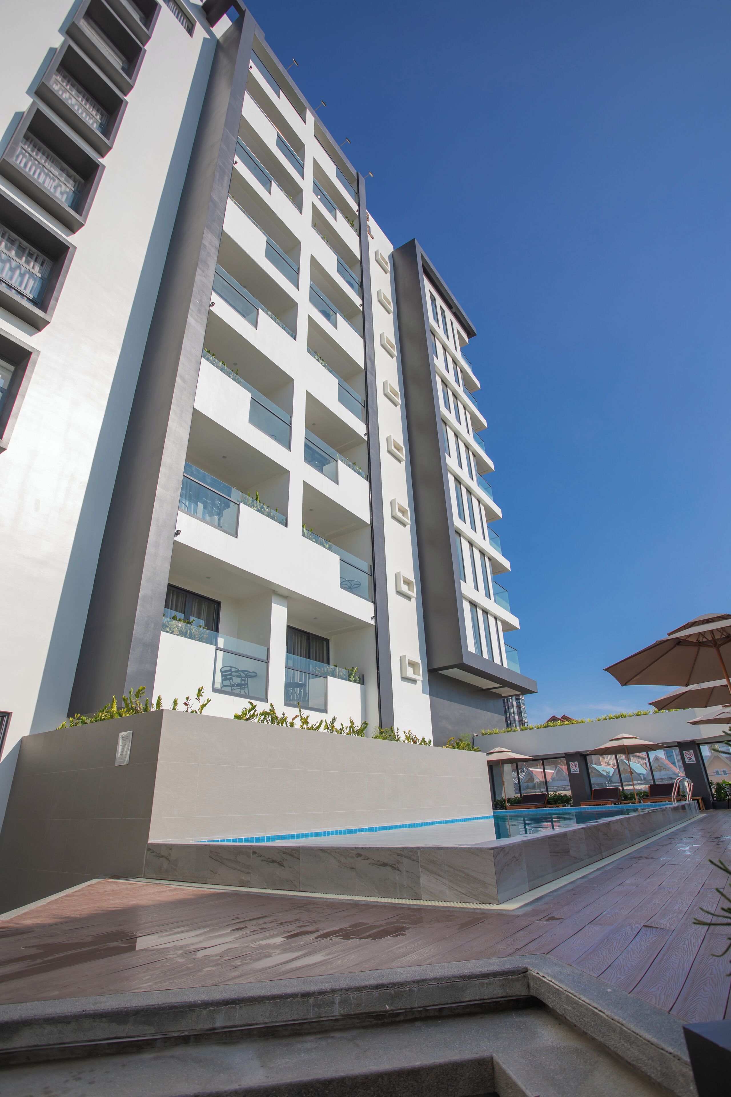 Un hotel moderno con varios pisos, piscina y mobiliario exterior.