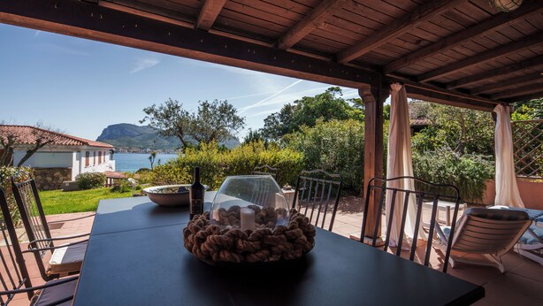A covered outdoor patio with a table, chairs, and a view of the sea.