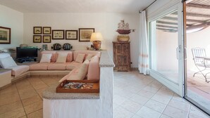 A living room with a pink sofa, a television, framed pictures on the wall, and a wooden cabinet.