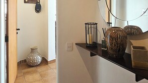 A hallway with a welcome mat, a mirror, a vase, and a shelf with decorative items. - Pitangueiras Mar Azul 🌊🌴 your cozy beachfront in Guarujá. (Barra Funda Guarujá)
