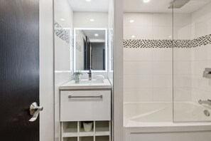 A modern bathroom with a glass shower enclosure, a white sink with a mirror, and a dark door. - Modern Mountain Home for 6 in Chateau Ridge (The Blue Mountains)