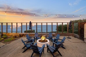 Eine Terrasse mit Feuerstelle, umgeben von Stühlen, mit Blick auf ein Gewässer.