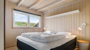 Een slaapkamer met een bed, houten wanden, een raam en twee wandlampen.