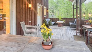 Eine Terrasse im Freien mit Holzmöbeln, einem Esstisch und einem Blumentopf mit gelben Blüten.