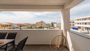 A balcony with a table and chairs, a wicker chair, and a view of surrounding buildings. - 2 bedroom awesome apartment in Povljana (Povljana)