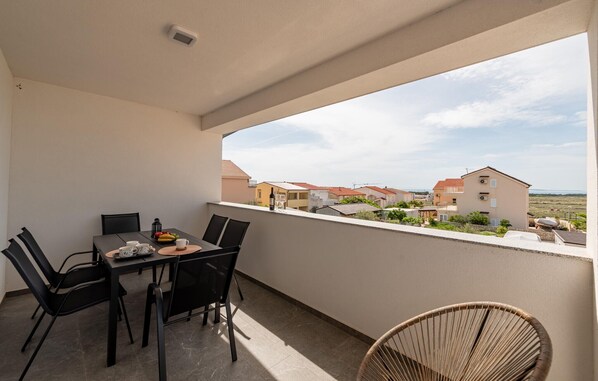 Ein Balkon mit Tisch für zwei Personen, Stühlen und einem Korbstuhl.