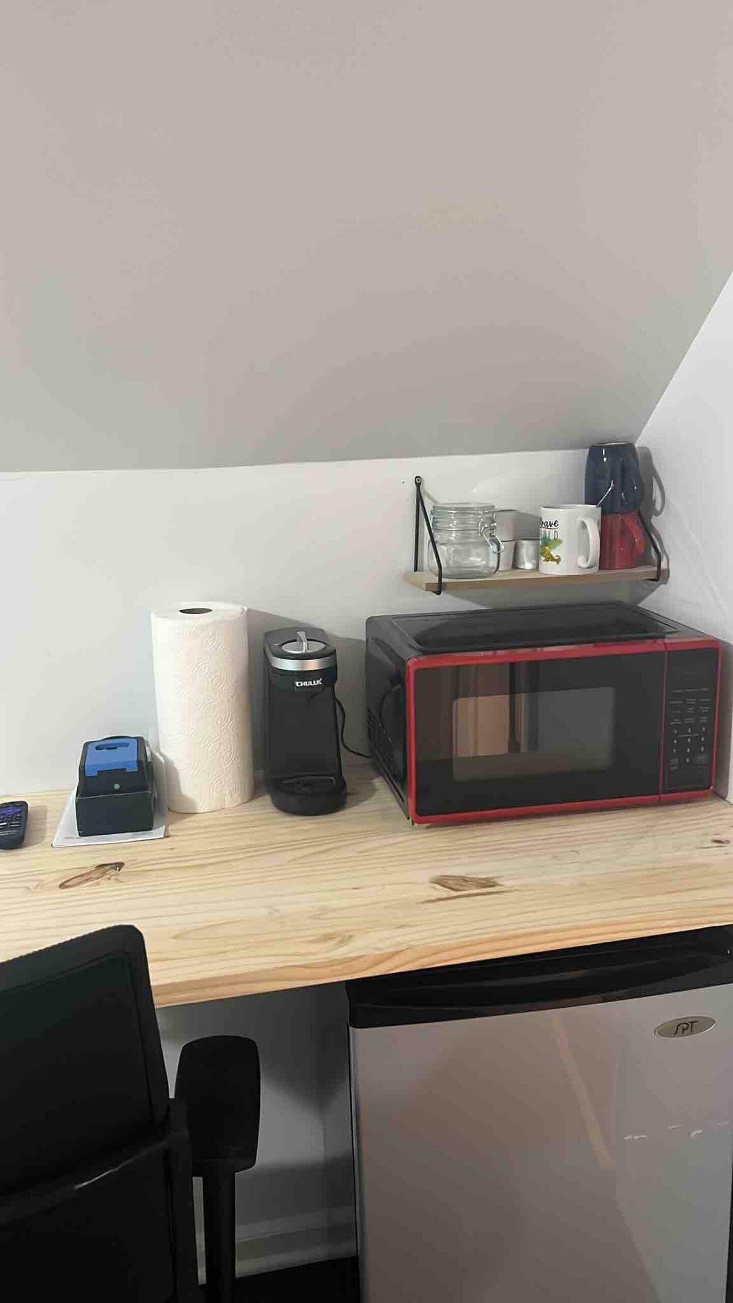 Eine Küchenzeile mit Mikrowelle, Kaffeemaschine und einer Rolle Küchenpapier auf einer Holz Arbeitsplatte.