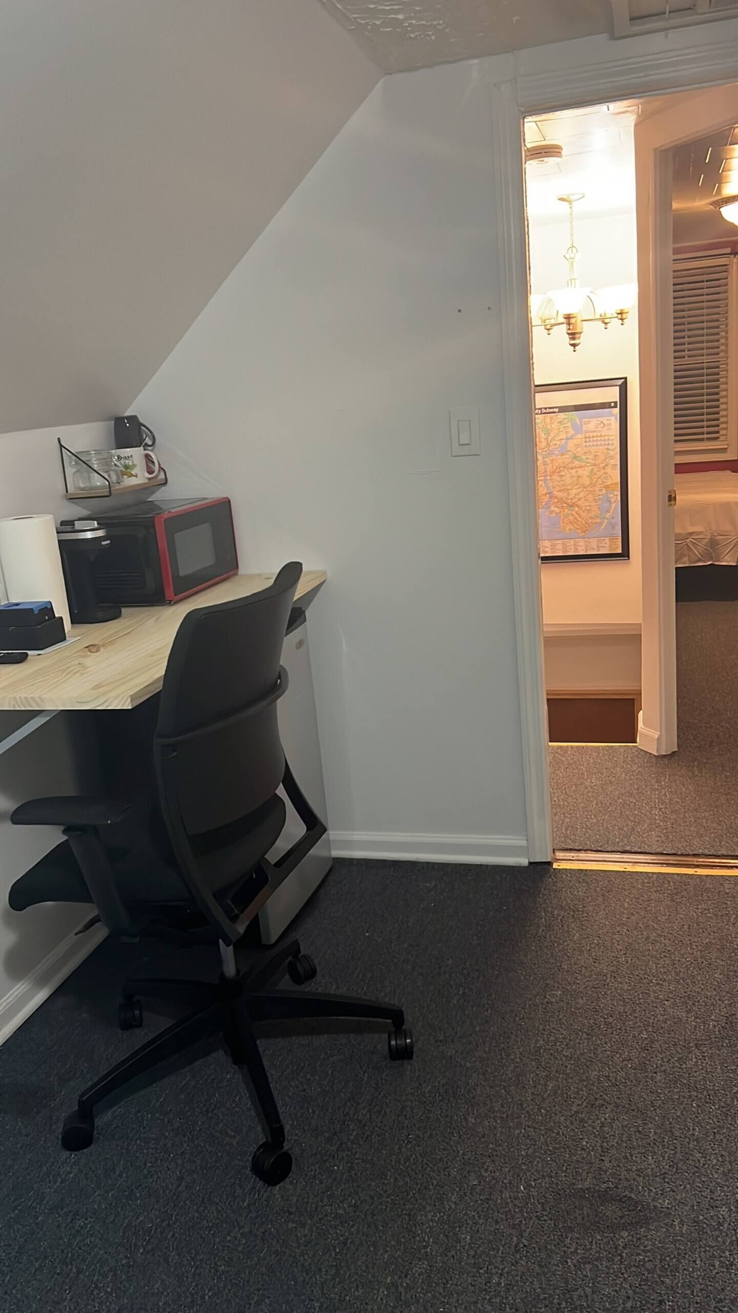 A small office space with a desk, chair, and a computer. There is a map on the wall and a lamp in the corner.