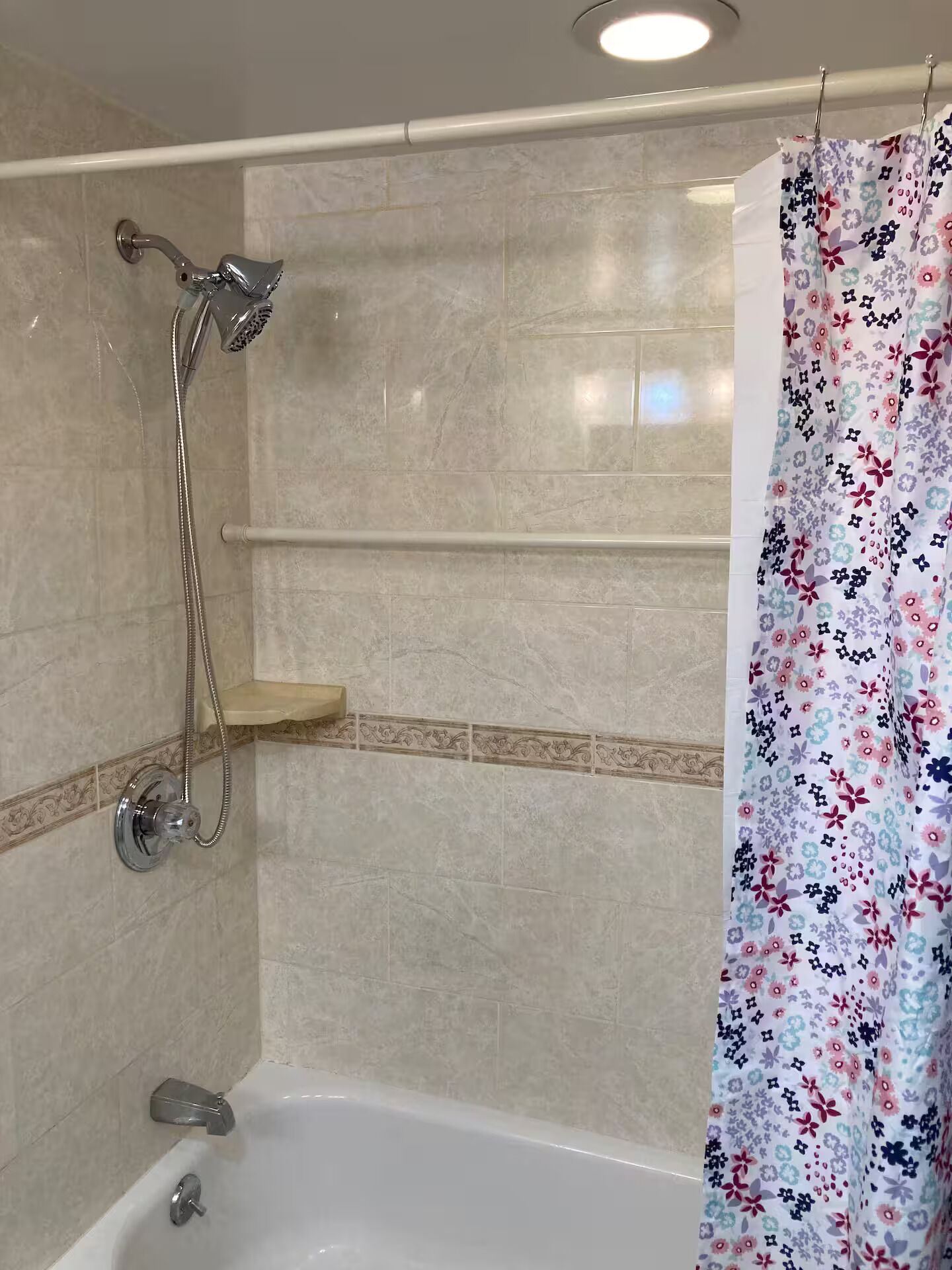 A bathroom with a bathtub, a shower with a handheld showerhead, and a floral shower curtain.