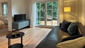 Una sala moderna con un sofá, un televisor, una mesita y un gran ventanal corredizo que da a un espacio al aire libre.