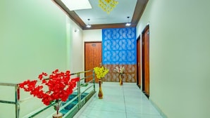 Un pasillo con piso de mármol, una escalera con barandilla de vidrio y un revestimiento de pared azul con diseño.