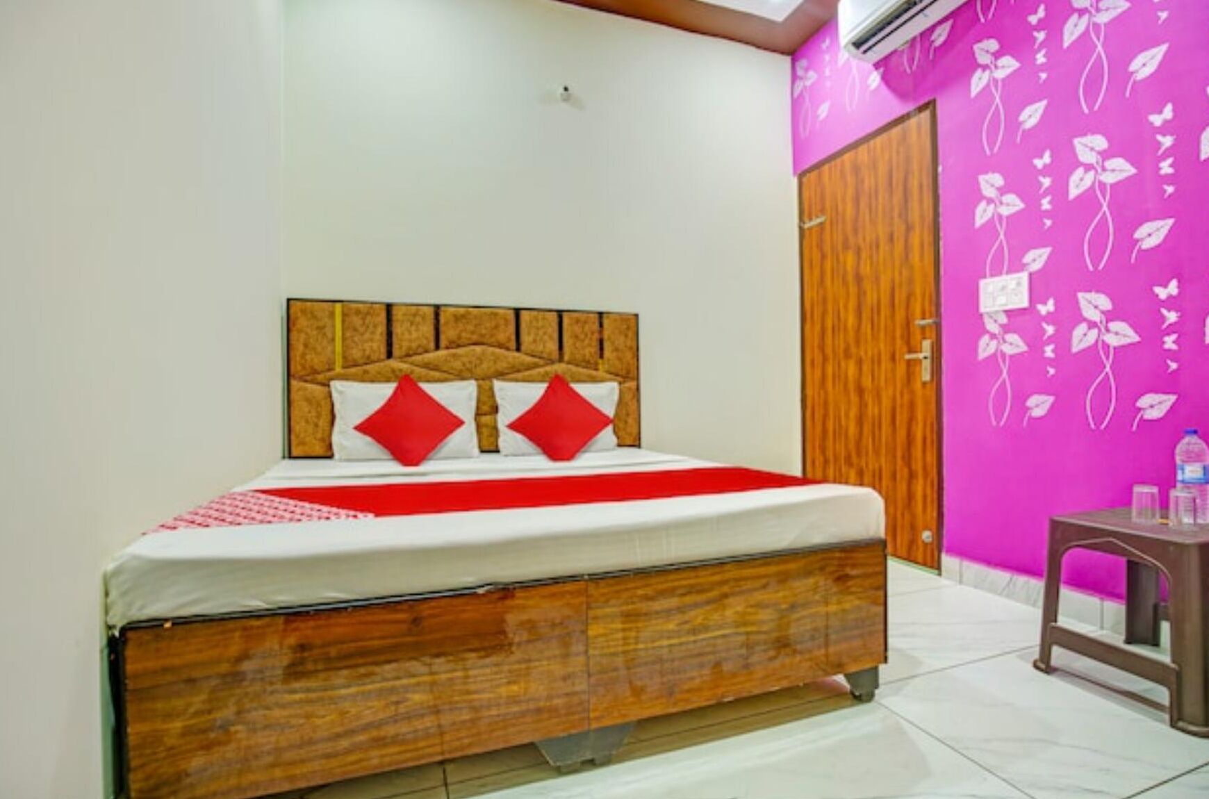 Un dormitorio con cabecero de madera, colcha roja y blanca, y pared rosa con motivos florales.