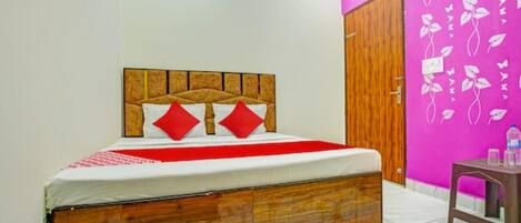 Un dormitorio con cabecero de madera, colcha roja y blanca, y pared rosa con motivos florales.