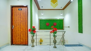 Zona de recepción con puerta de madera con la etiqueta 107, pared verde con un cuadro enmarcado y dos jarrones con flores rojas.