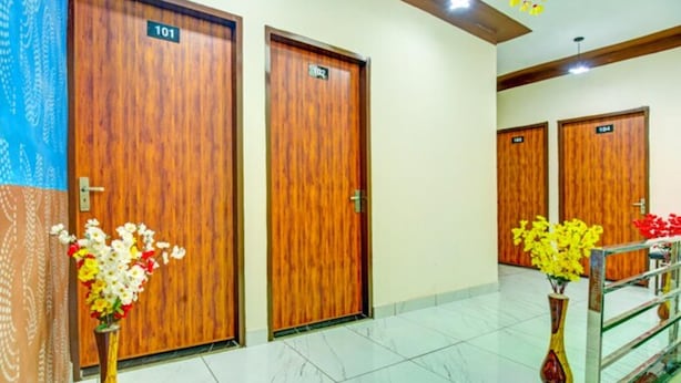 Un vestíbulo de hotel con puertas de madera numeradas 101 y 102, suelo de mármol y arreglos florales.