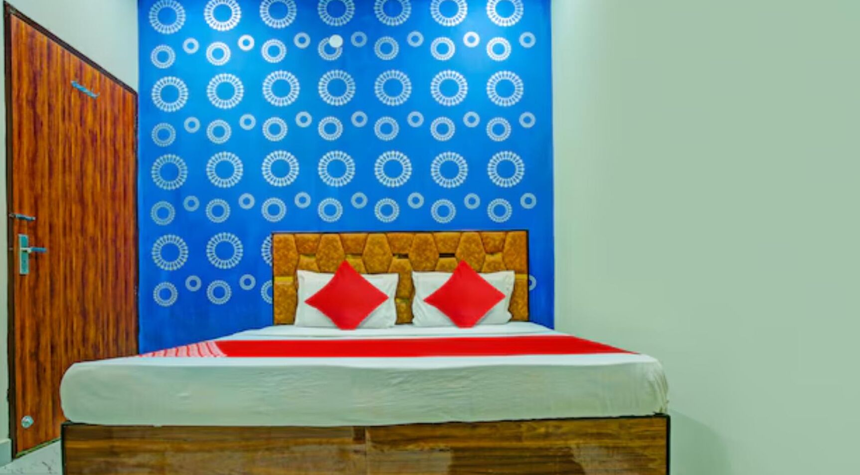 Une chambre à coucher avec une tête de lit en bois, un lit avec une literie rouge et blanche, et un mur bleu orné de motifs circulaires.