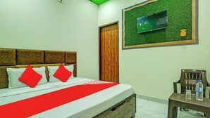Una habitación de hotel con una cama, un televisor montado en una pared verde, una puerta de madera y una mesita con una botella.