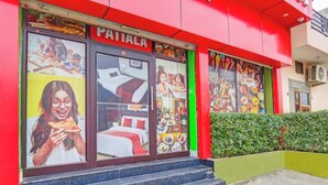 Fachada roja de un hotel, con múltiples ventanas que muestran el interior y un conjunto de escaleras que conducen a la entrada.